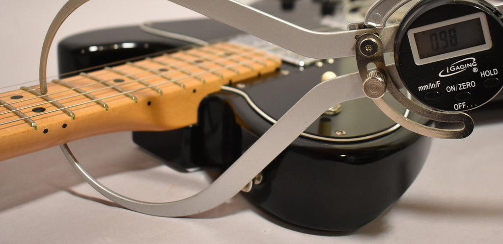 A digital fret height gauge measures the black guitar's maple neck and fretboard, showing a reading of 0.98.