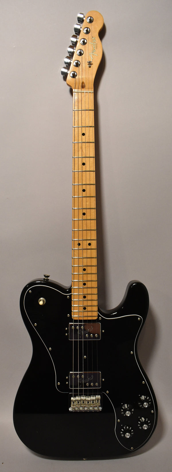 Full-length view of a glossy black Telecaster with a maple neck, two humbuckers, and four chrome control knobs on a white pickguard.