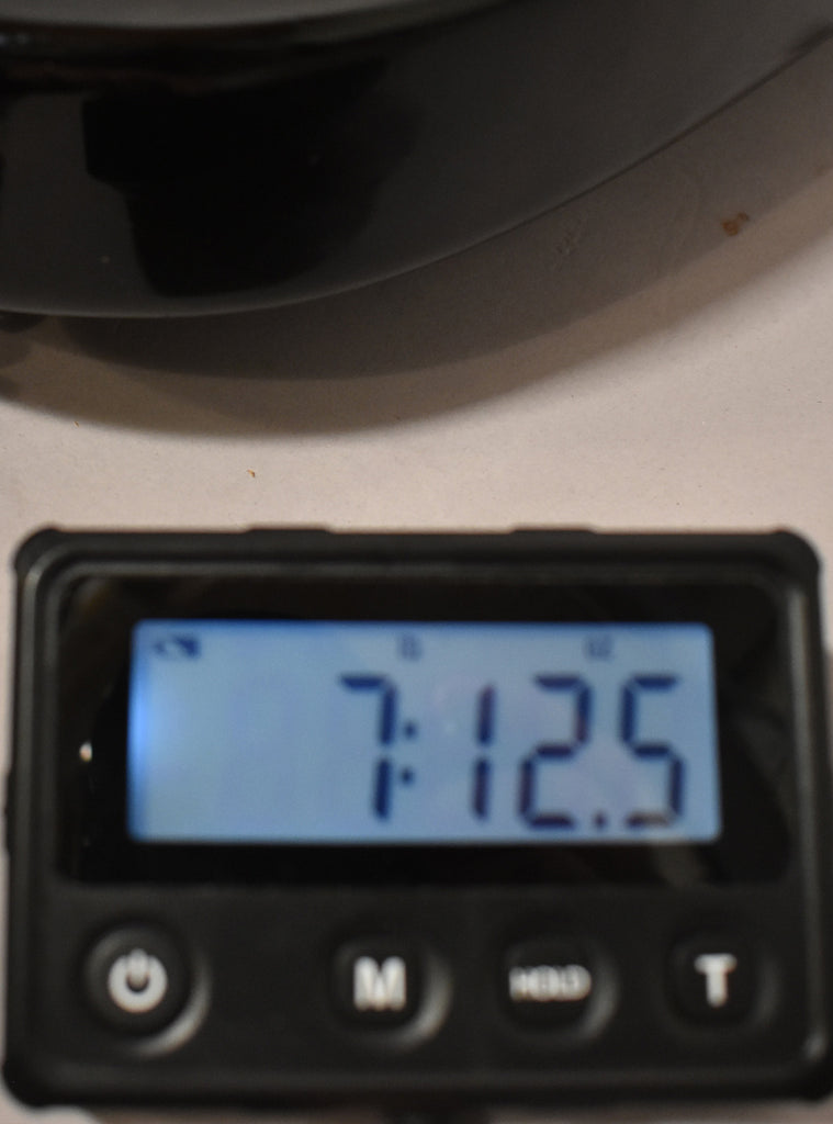 A close-up of a digital scale displaying "7:12.5" in blue, with power, M, MODE, and T buttons below.