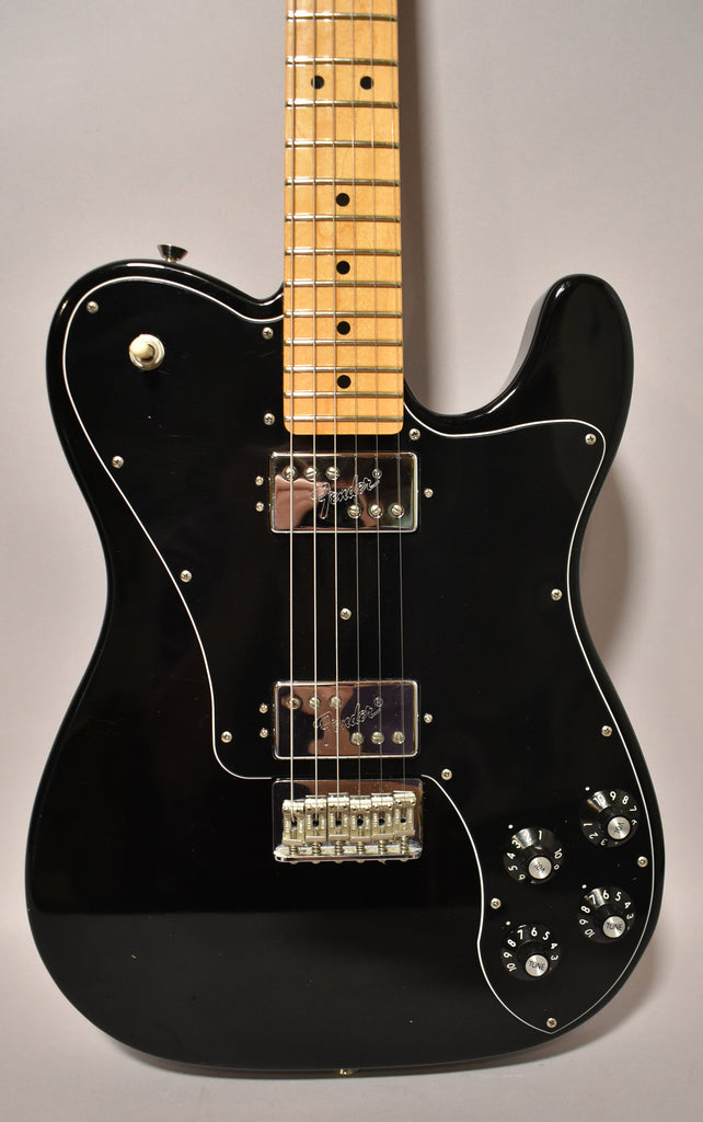 Full-frame view of a black Telecaster Deluxe with a maple fretboard, two chrome humbuckers, and four black control knobs.