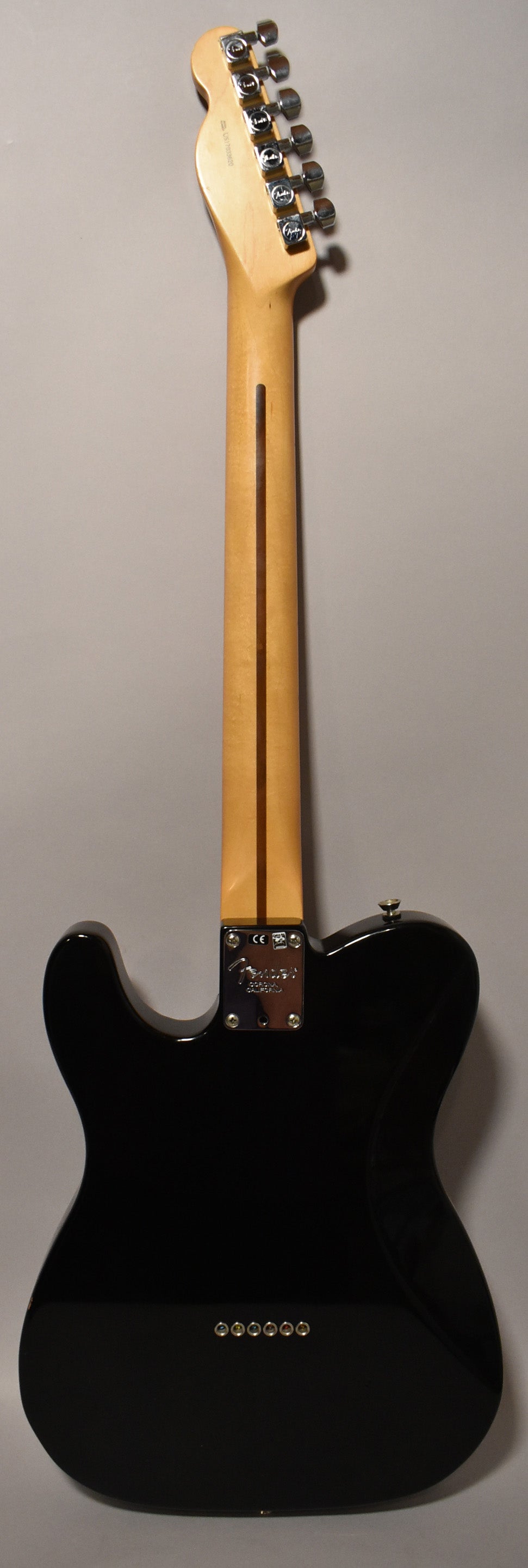 The back of a glossy black Telecaster, showing a light wood neck, chrome tuners, and six string ferrules on the body.
