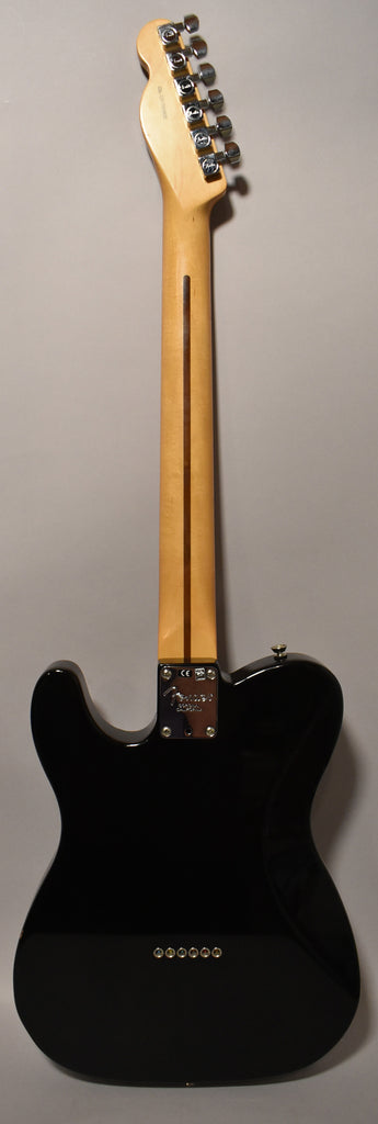 The back of a glossy black Telecaster, showing a light wood neck, chrome tuners, and six string ferrules on the body.