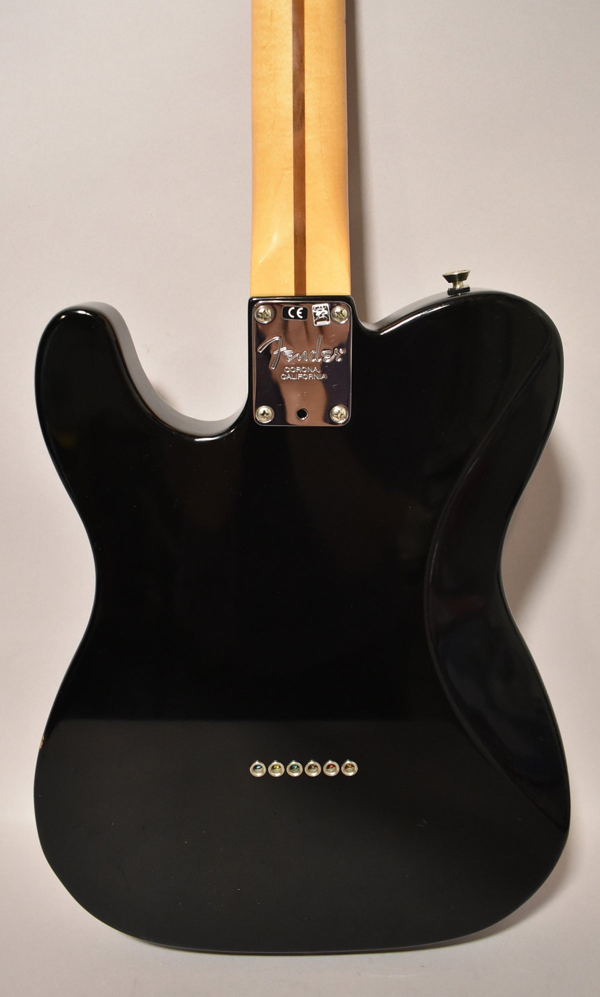 Rear view of a glossy black electric guitar, showing the neck plate, light wood neck, and six string ferrules.
