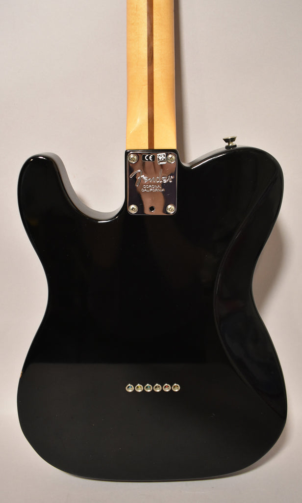 Rear view of a glossy black electric guitar, showing the neck plate, light wood neck, and six string ferrules.