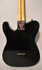 Rear view of a glossy black electric guitar, showing the neck plate, light wood neck, and six string ferrules.