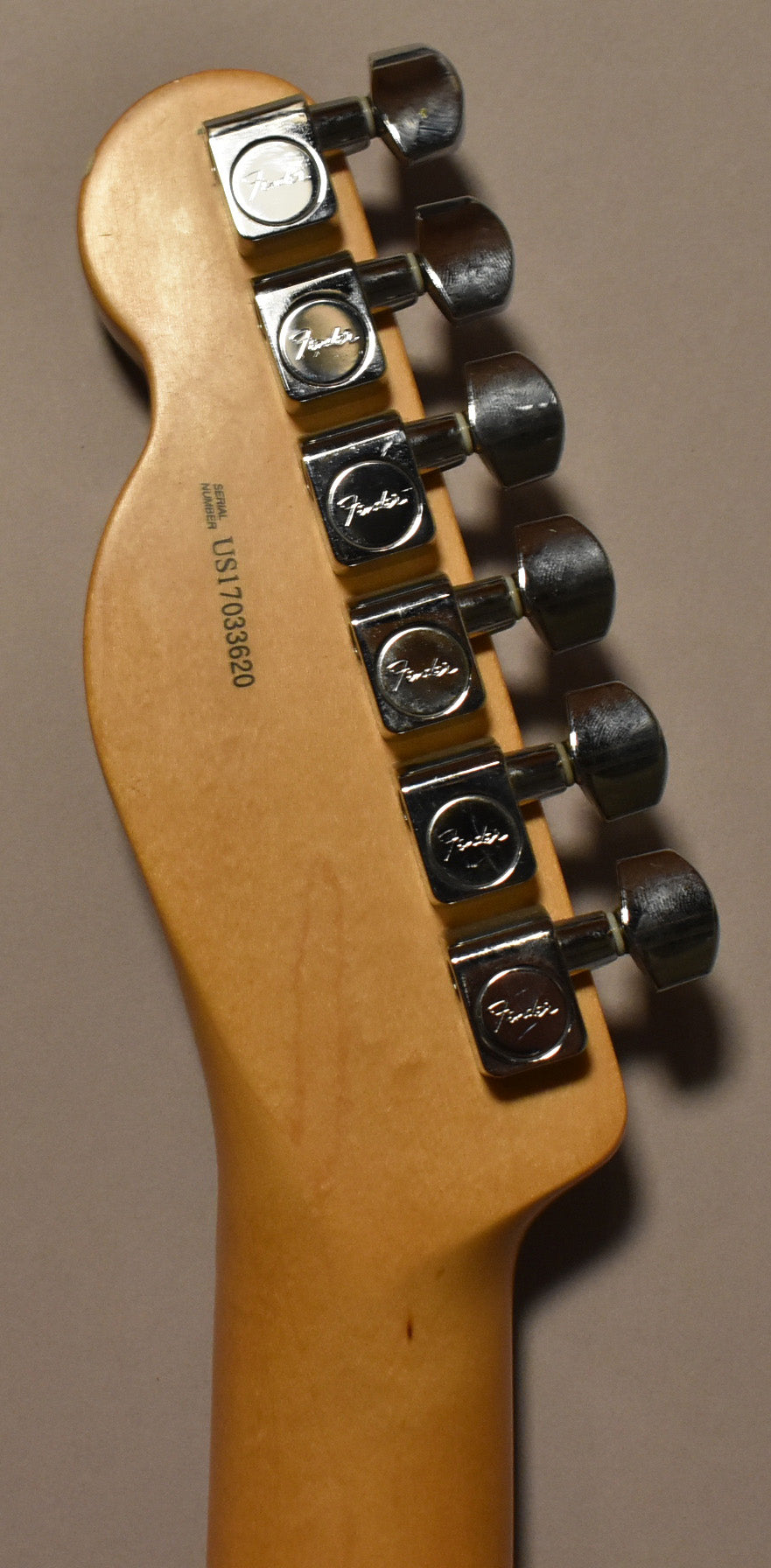 Close-up of the guitar's natural wood headstock and neck, showing six chrome tuning machines with light wear and a serial number.