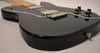 The black Telecaster body is angled from the lower bout, showing the output jack, four black control knobs, and two humbuckers.