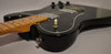 Close-up of a glossy black Telecaster body with a cream toggle switch, chrome hardware, and a maple neck.
