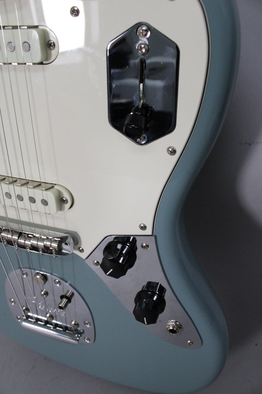 Close-up of the Sonic Grey Jaguar's lower body, showing the white pickguard, chrome control plates, black knobs, and bridge.