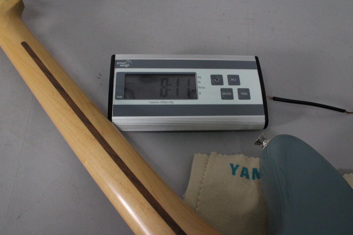 The guitar's light wood neck with a dark stripe is angled across the frame, with a digital scale displaying "8:11" in the background.