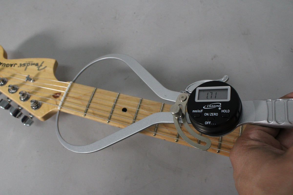 A hand holds a digital caliper measuring the nut width of a Fender Jaguar guitar neck, displaying "1.71".