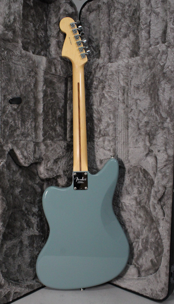 Full rear view of a glossy sonic grey Jaguar electric guitar with a light maple neck and chrome tuners, resting in a grey plush case.
