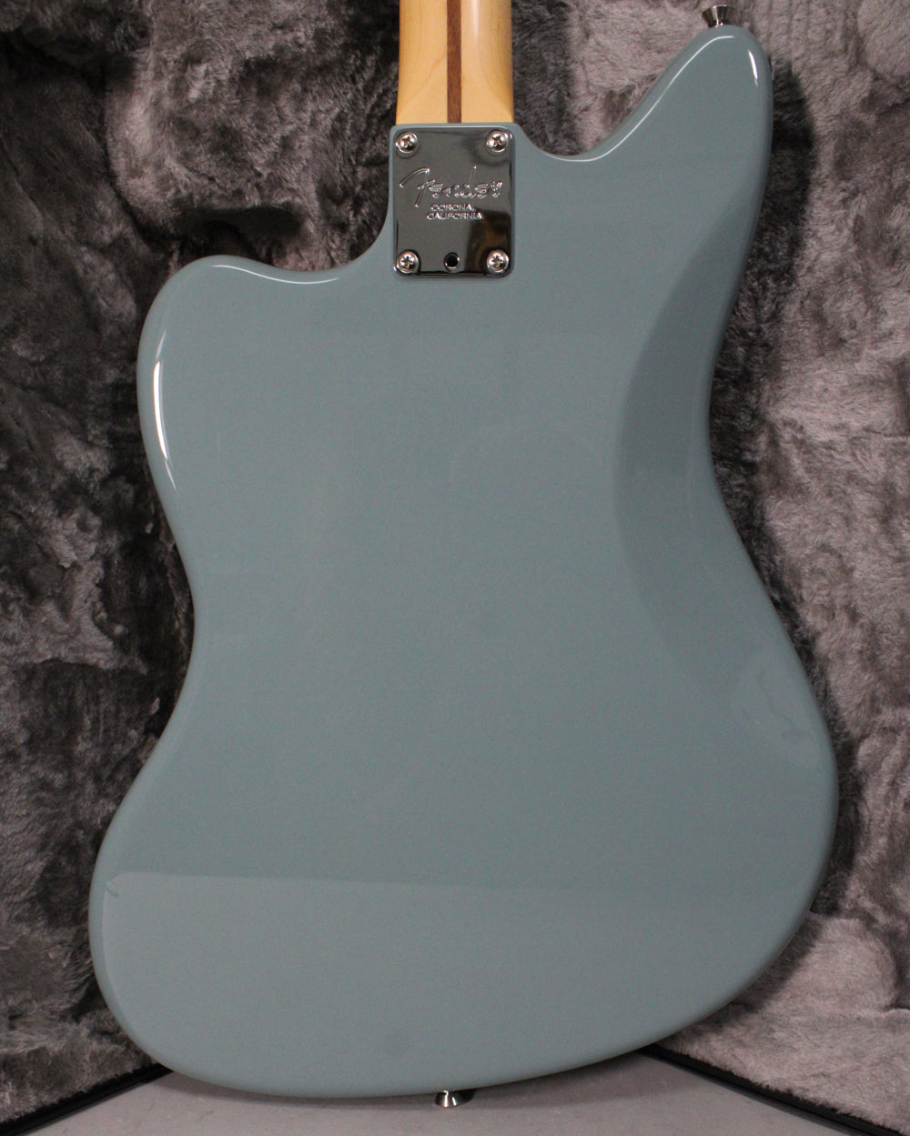 The back of a sonic grey Jaguar electric guitar, showing the neck plate and a light-colored maple neck.