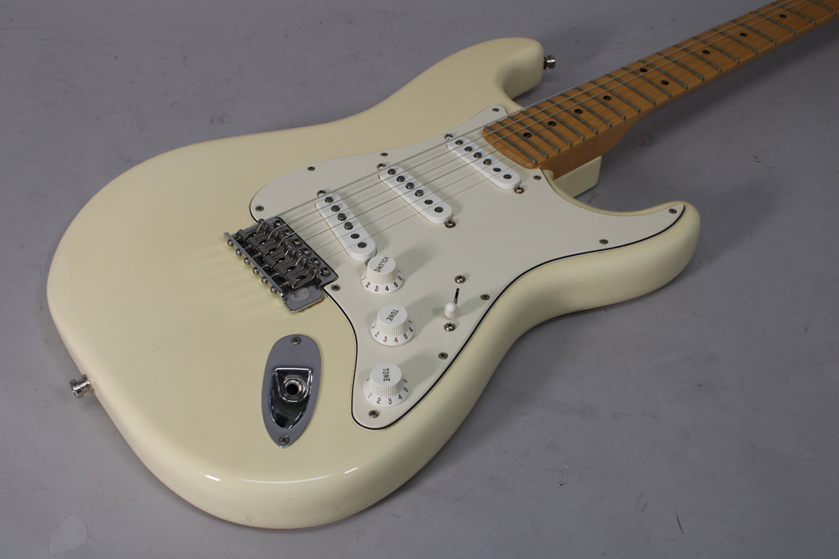 Olympic White Stratocaster, angled from above, showing the body, white pickguard, three single-coil pickups, and maple fretboard.