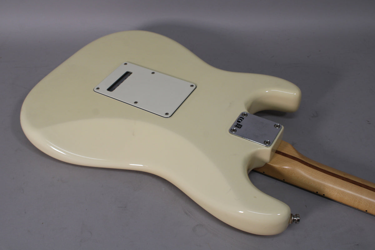 The back of an off-white Stratocaster body, showing the tremolo cavity cover, neck plate, and part of the light wood neck.