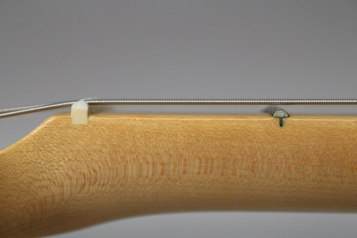 Close-up of the light maple neck and fretboard, showing the nut and a string tree, with subtle wood grain visible.