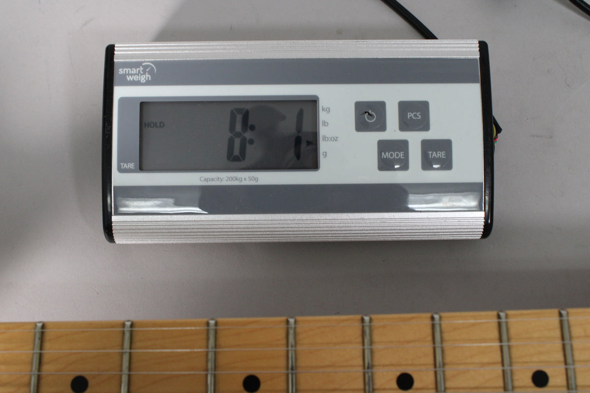 Close-up of a digital scale displaying "8.1" kg, with a maple fretboard and frets visible below.