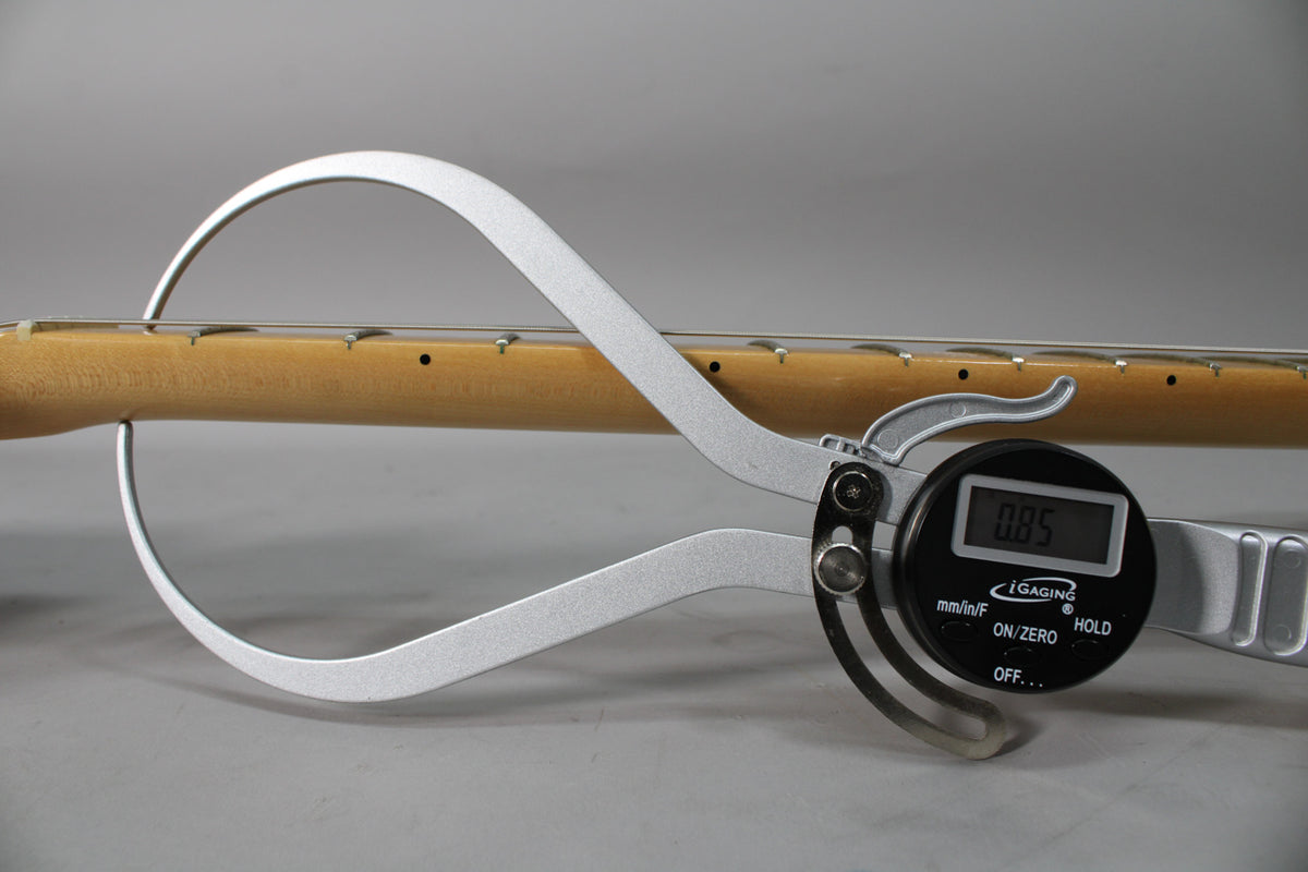 A digital caliper measures the guitar neck, displaying "0.85" on its screen.