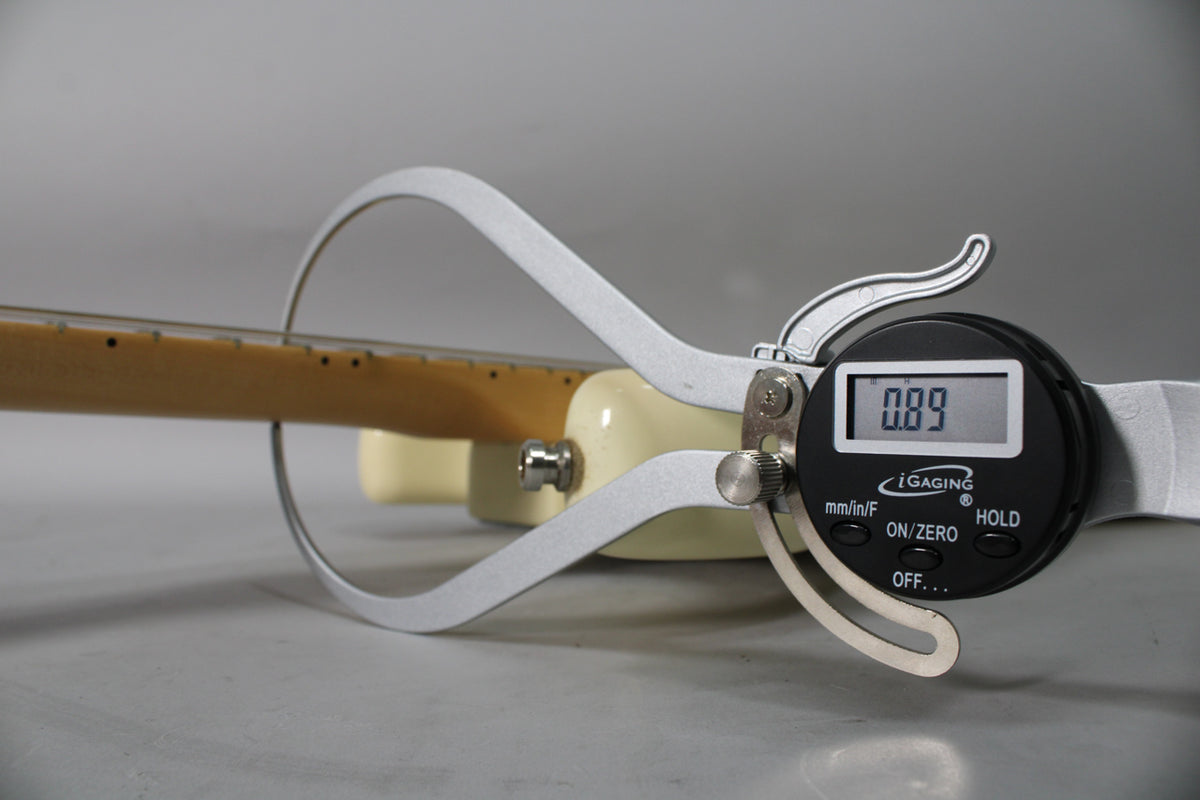 A digital caliper measures the neck relief of the Olympic White Stratocaster, displaying "0.89" on its screen.
