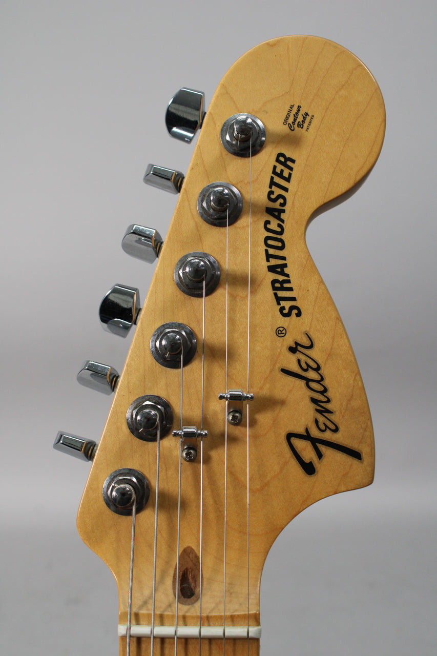 Close-up of the light-colored maple headstock with six chrome tuners, two string trees, and a visible wood knot near the nut.