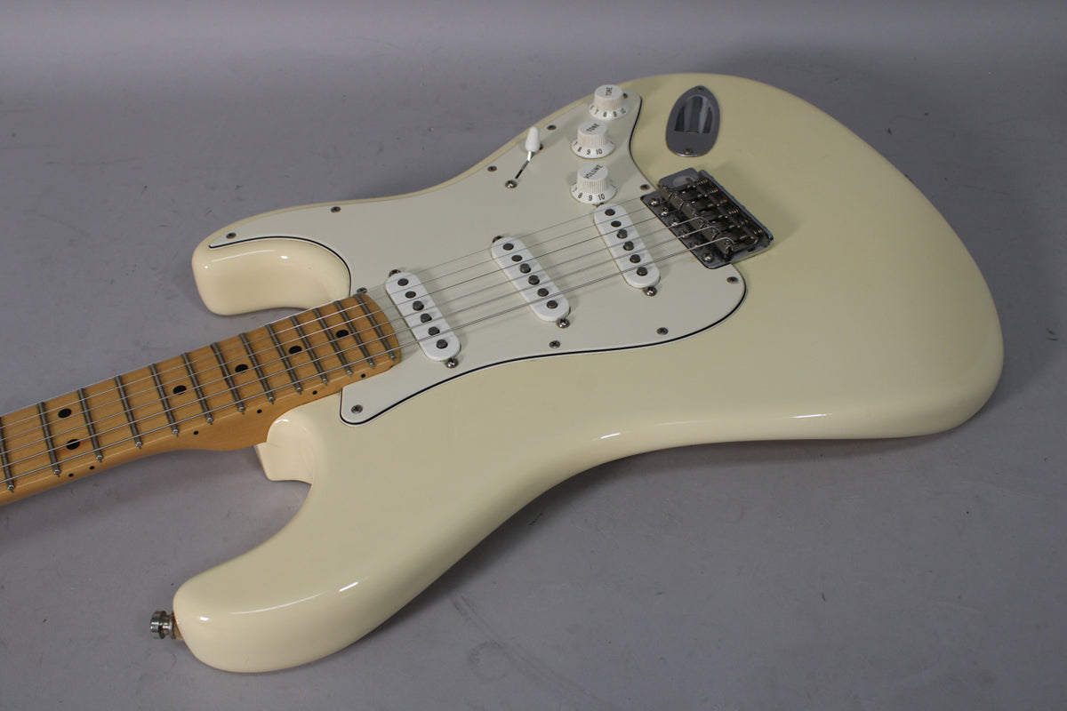 An Olympic White Stratocaster, angled from the lower left, showing the maple neck, white pickguard, three single-coil pickups, and chrome hardware.