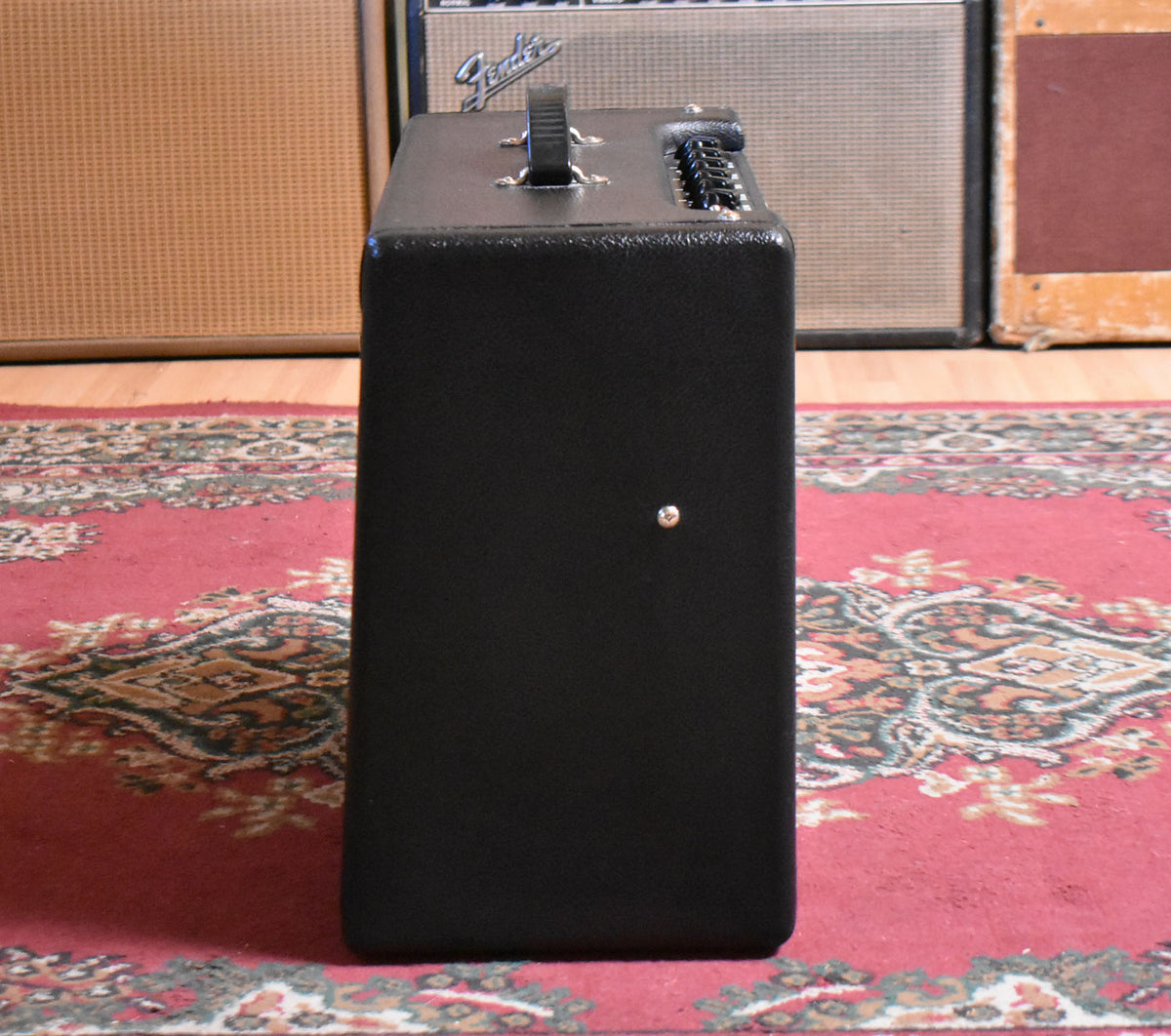 The black tolex combo amp is shown from the right side, revealing a single silver button on the side and top-mounted controls.