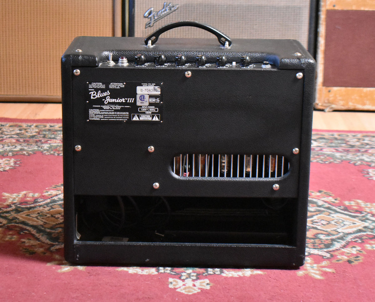 Rear view of a black combo amp with a top handle, showing the control panel, a vented tube section, and an open lower back.