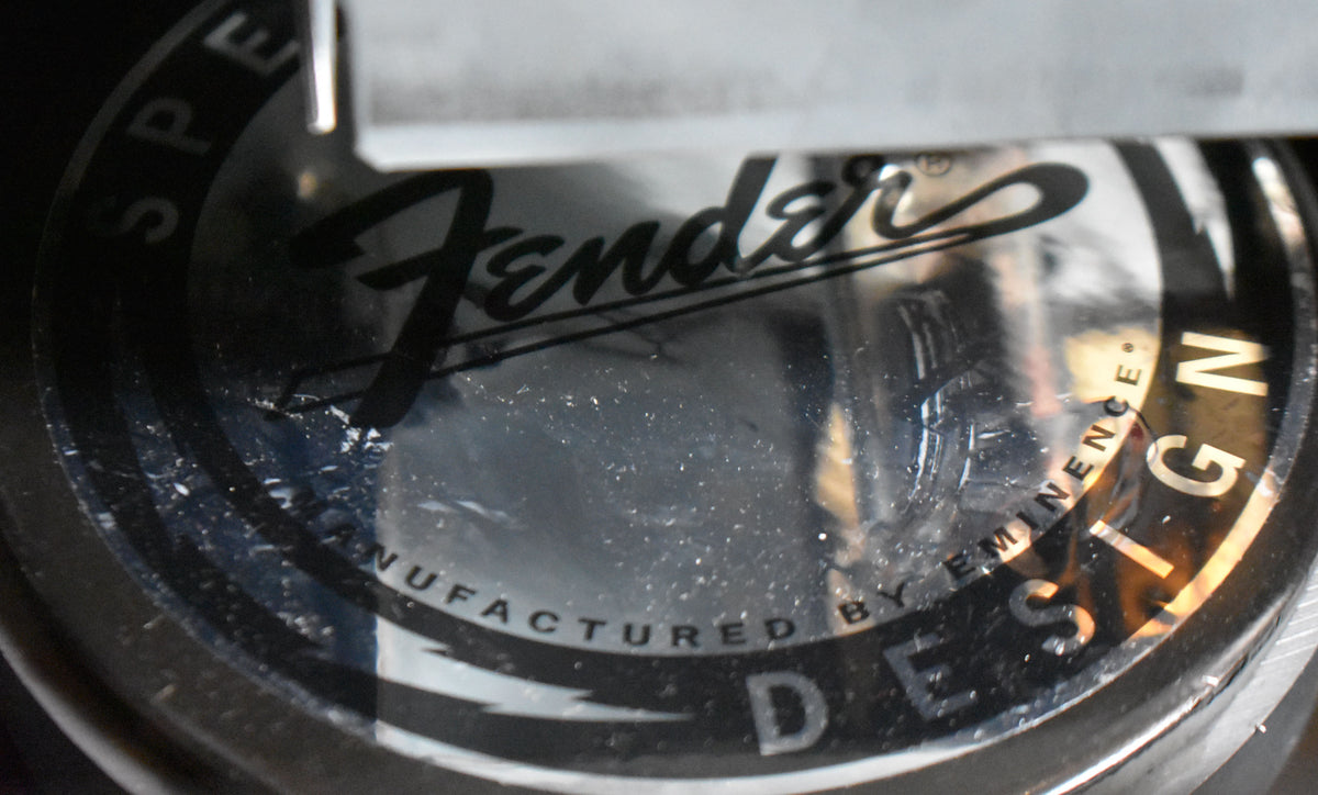 Close-up of the speaker's shiny black dust cap, showing the Fender logo and "Manufactured by Eminence" in white text, with light scuffs.