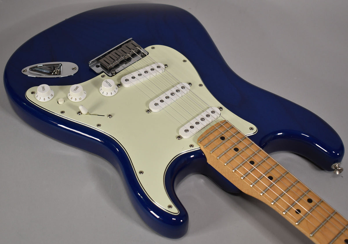 Sapphire blue electric guitar, angled from above, showing the body, white pickguard, three single-coil pickups, and maple fretboard.