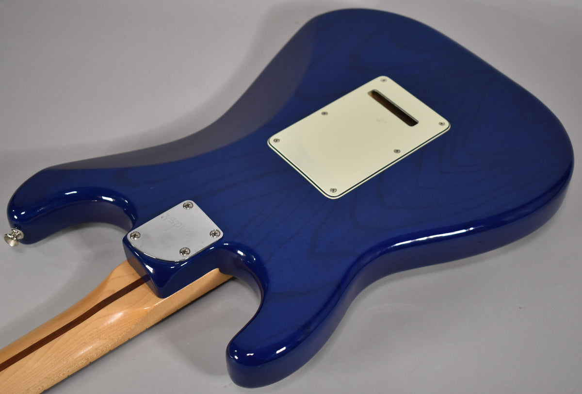 Rear view of a sapphire blue Stratocaster body, showing the light cream tremolo cover, chrome neck plate, and light maple neck.