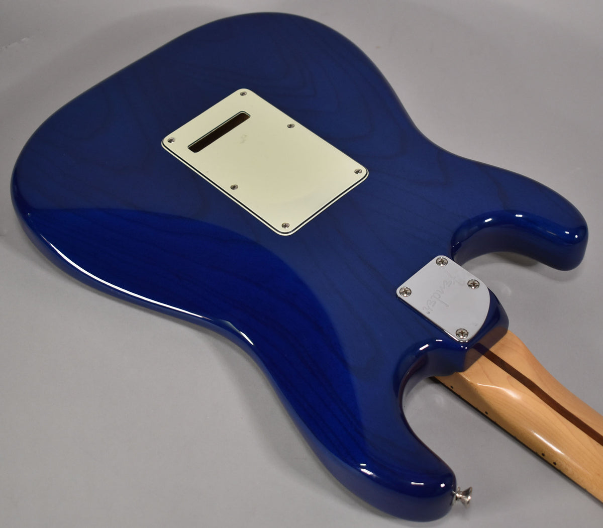 The back of a sapphire blue Stratocaster, showing the cream tremolo cover, chrome neck plate, and a light maple neck.