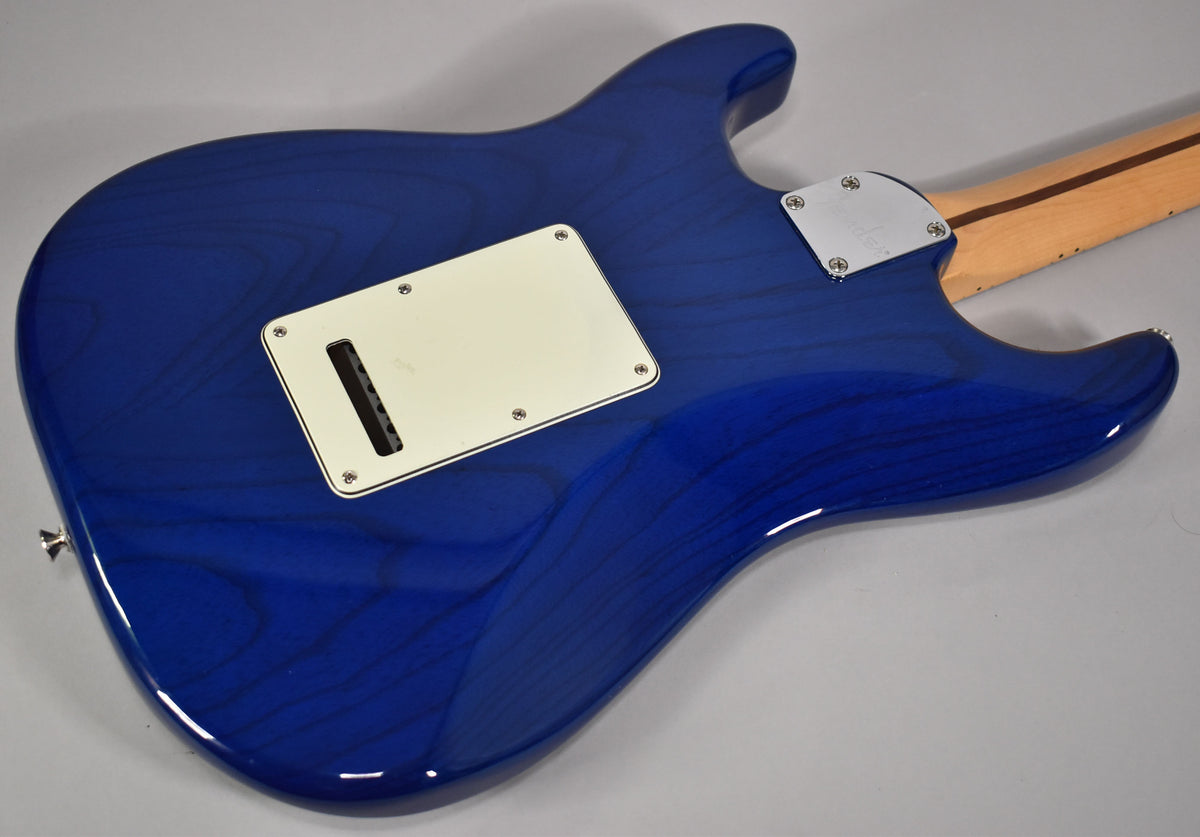 The back of a sapphire blue electric guitar, showing the wood grain through the glossy finish, with a cream tremolo cover.