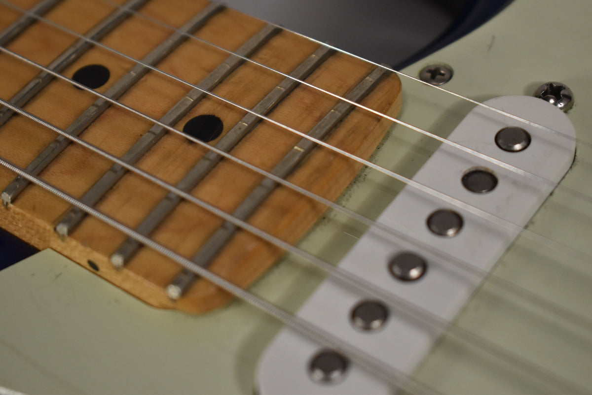 Close-up of the maple fretboard with black dot inlays, six strings, and a white single-coil pickup with exposed pole pieces.
