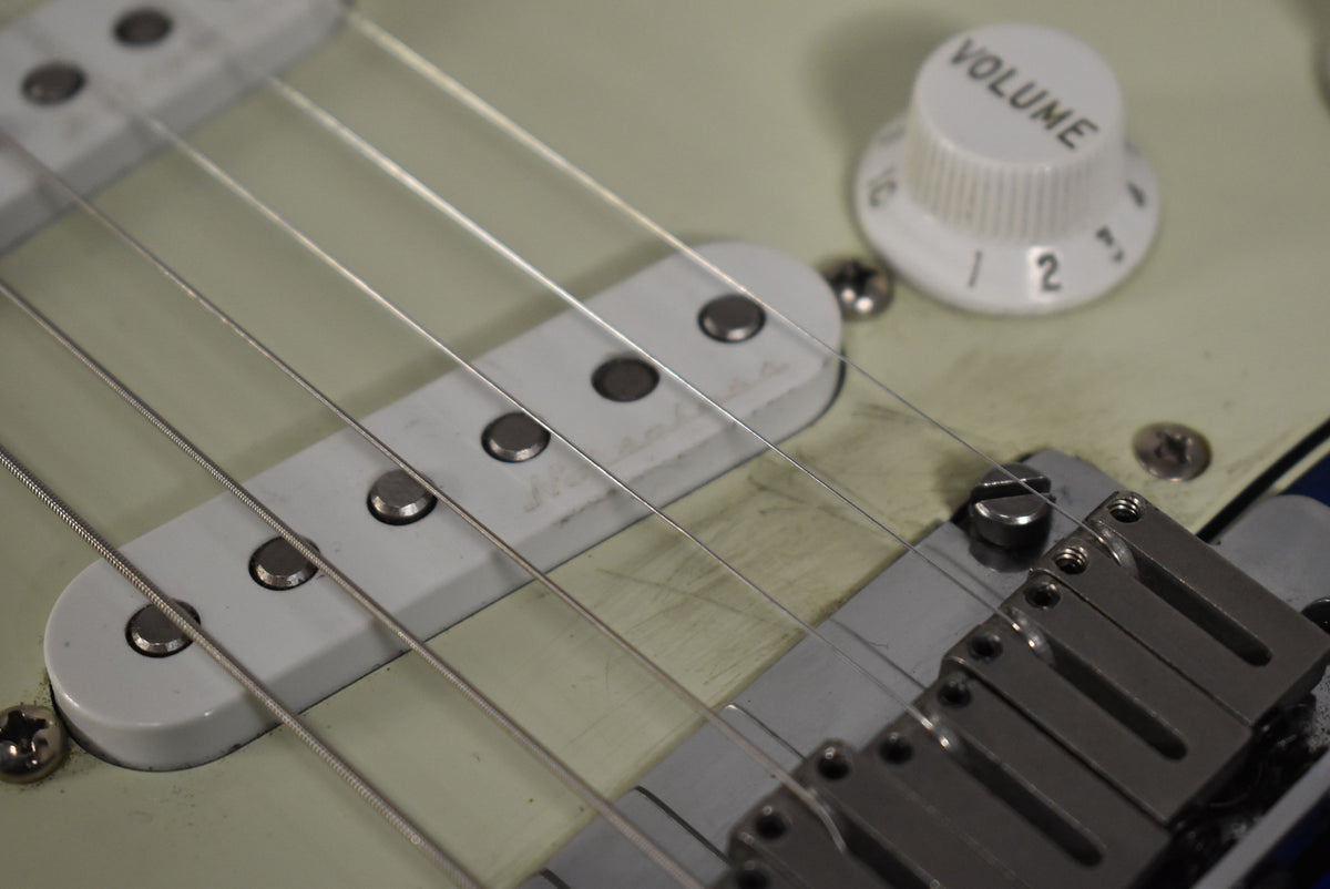 Close-up of the guitar's lower body, showing the bridge, middle pickup, and a white "VOLUME" knob on a cream pickguard.