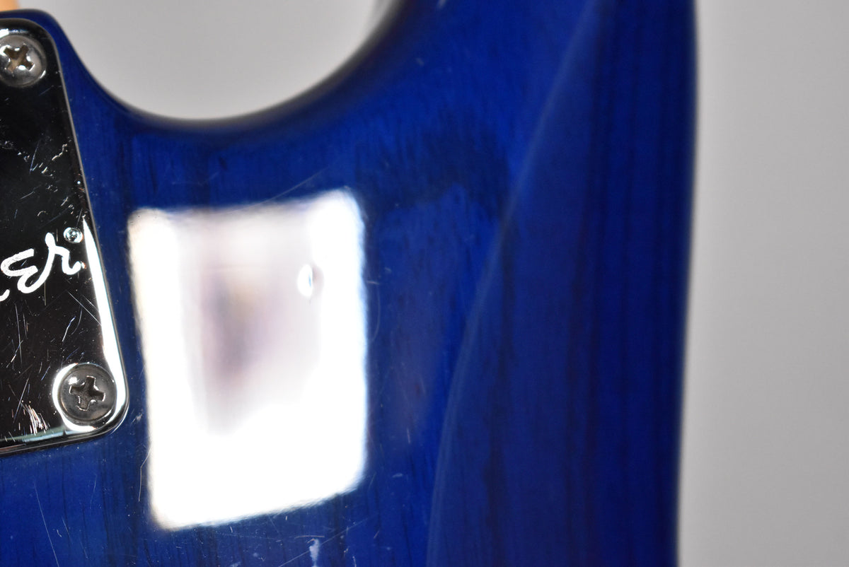 Close-up of the sapphire blue body near the neck plate, showing light scratches and a small ding on the glossy finish.