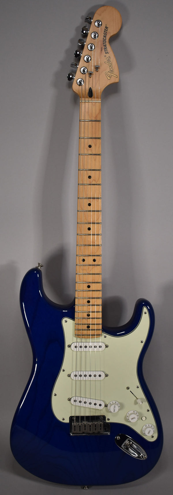 Full-length, front view of a glossy sapphire blue Stratocaster with a maple fretboard, cream pickguard, and three single-coil pickups.