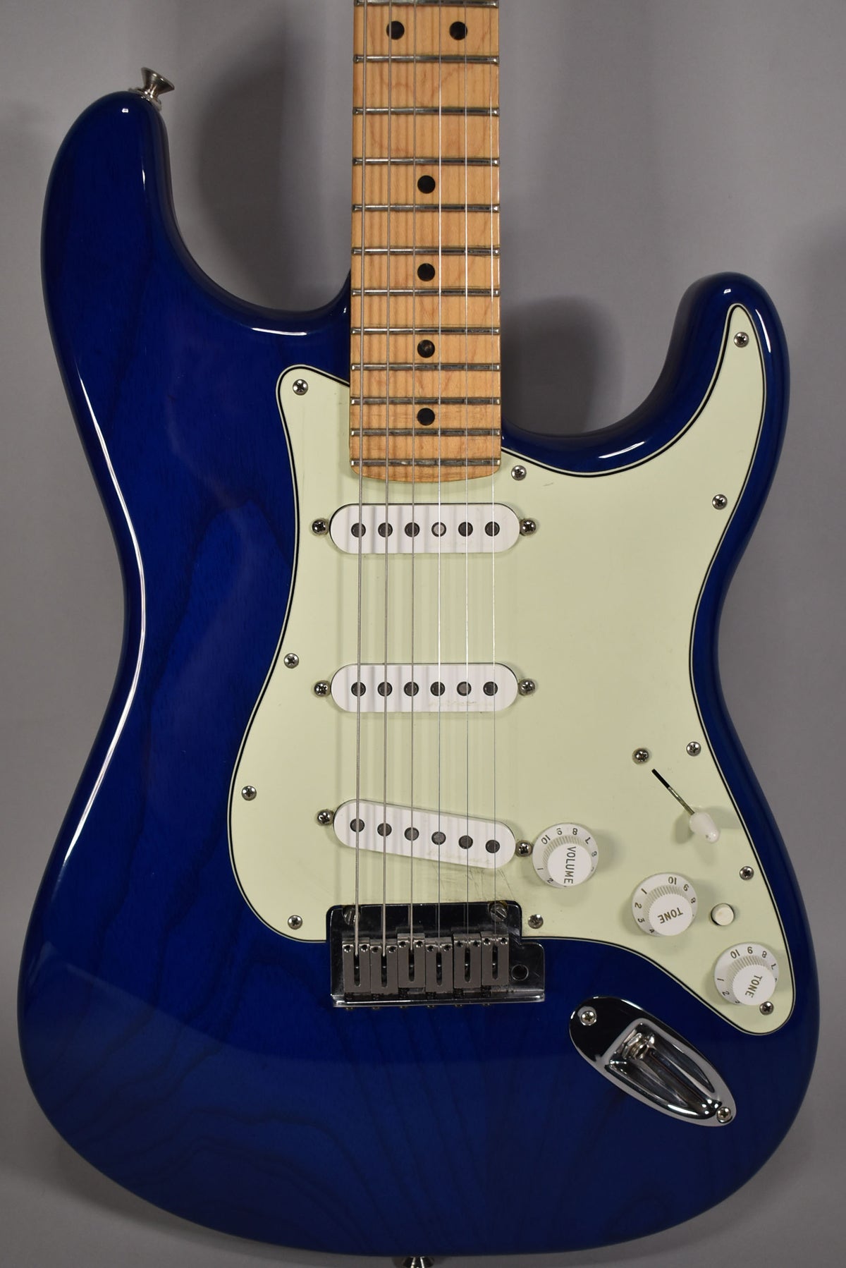 Full-frame, glossy sapphire blue electric guitar with a light maple fretboard, cream pickguard, three single-coil pickups, and chrome hardware.