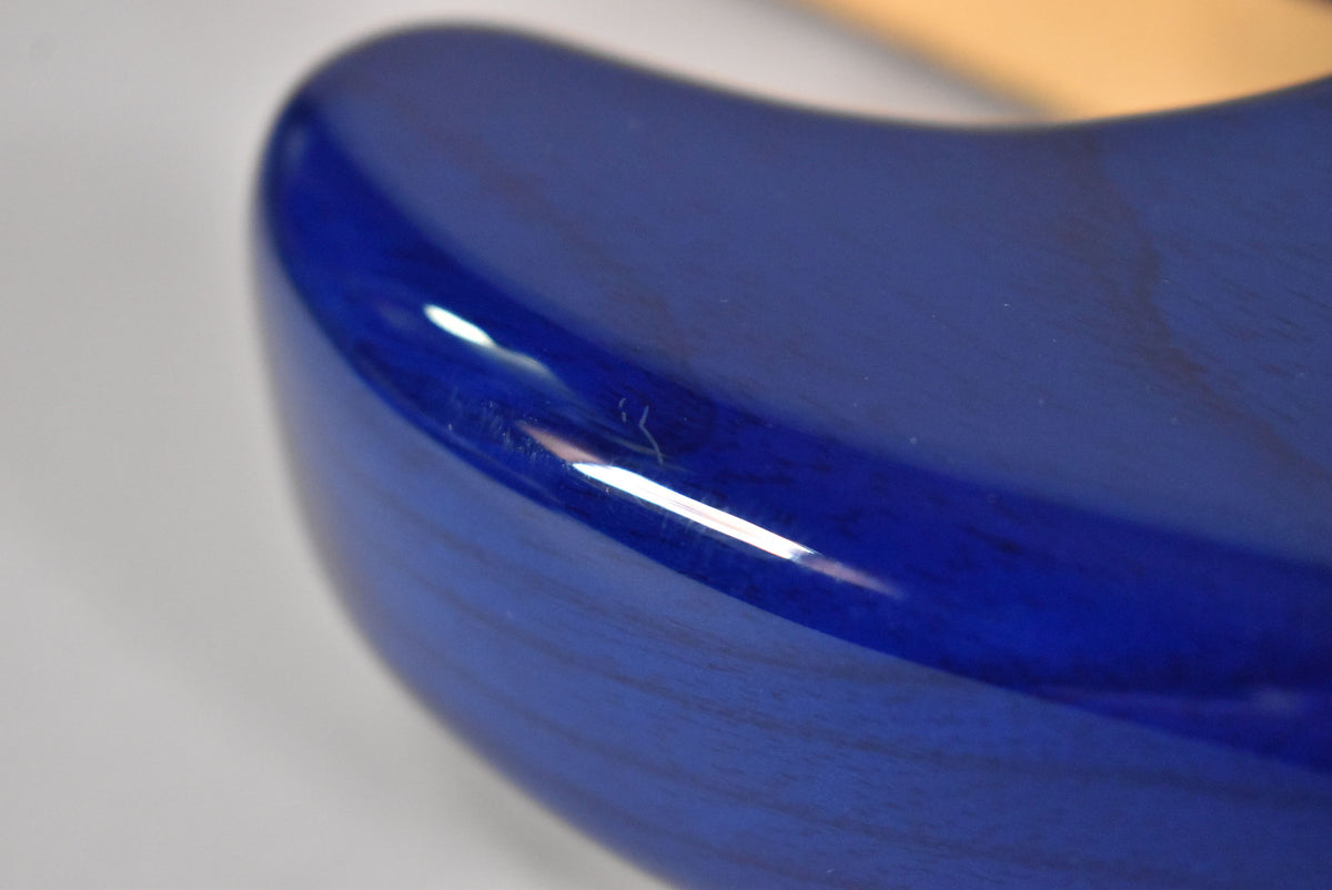 Close-up of the guitar's sapphire blue body, showing a small scratch on the upper bout and the wood grain visible through the finish.