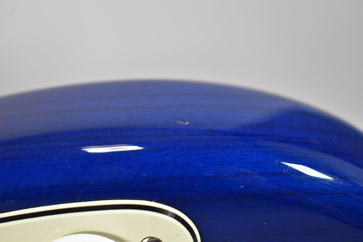 Close-up of the sapphire blue guitar body, showing a small ding in the finish above the cream-colored pickguard.