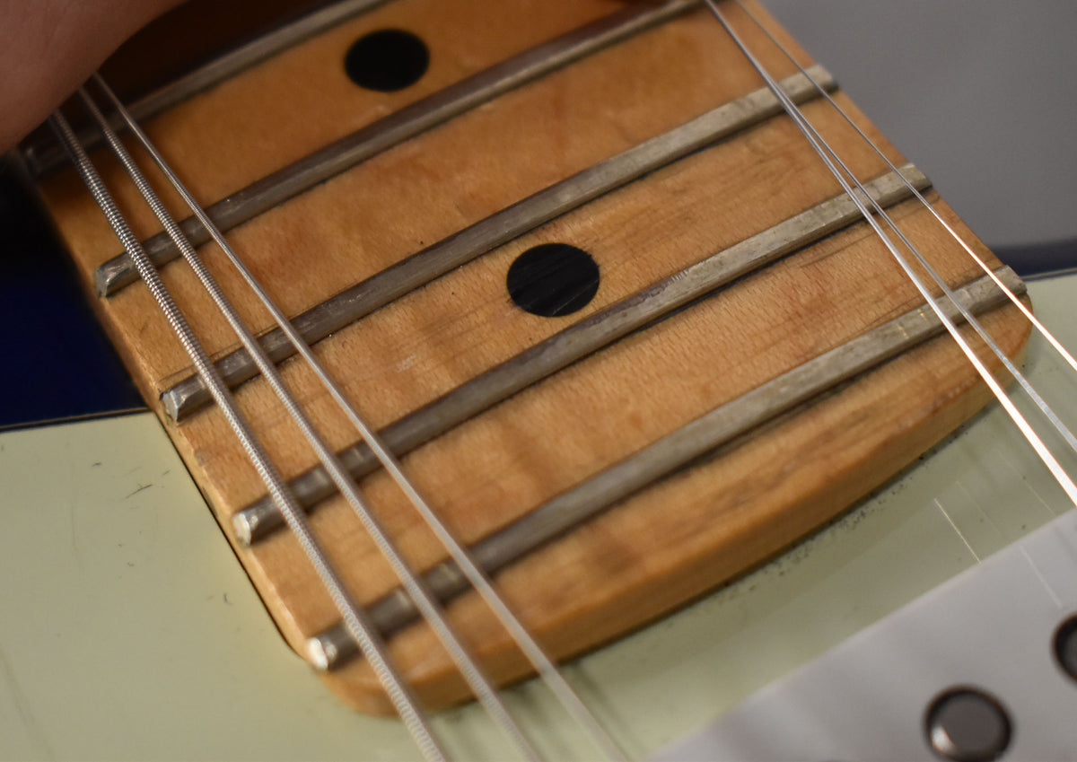 Close-up of the maple fretboard with dark circular inlays, showing light wear on the frets and the edge of a mint green pickguard.