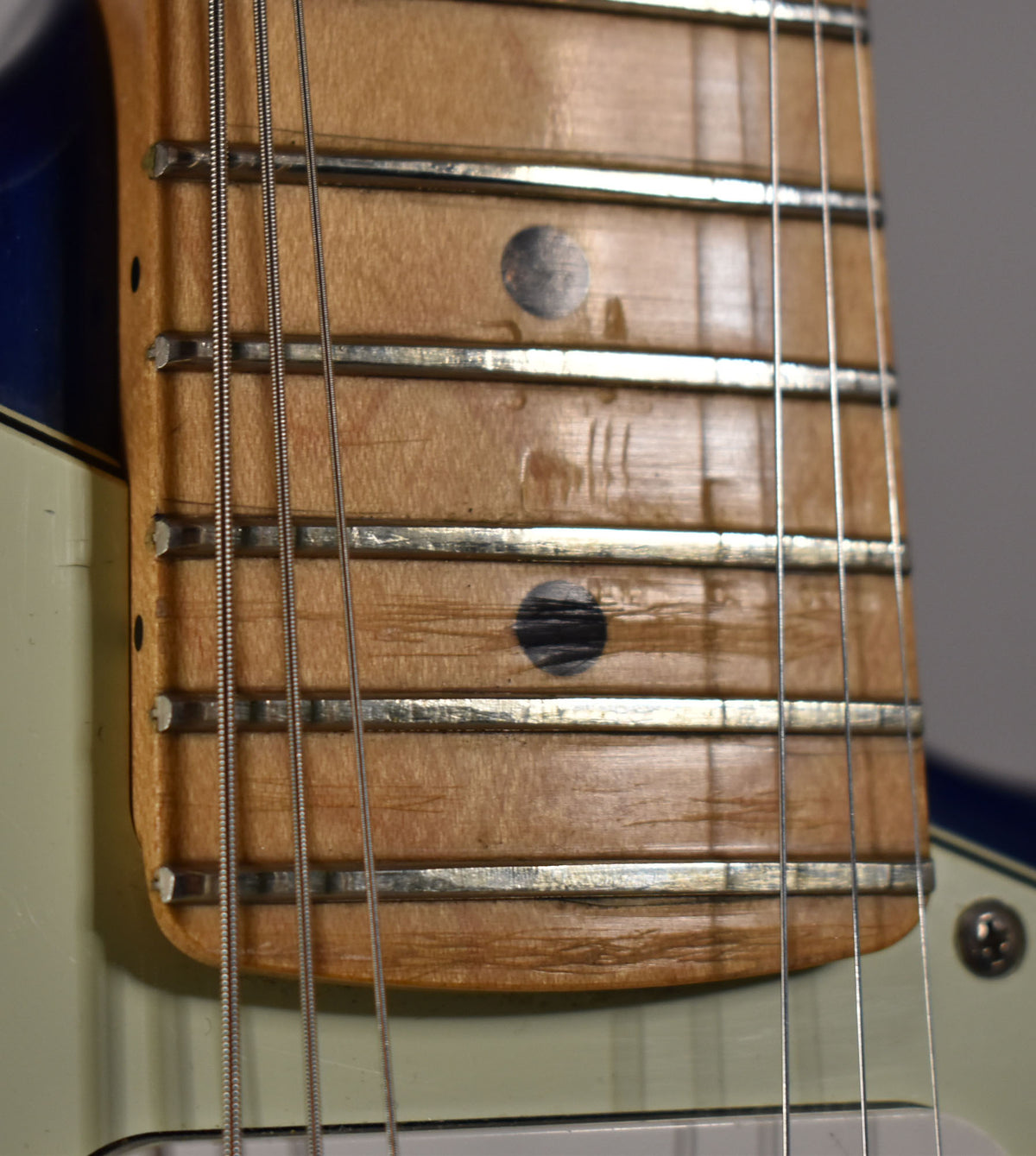 Close-up of the maple fretboard with dark circular inlays, showing visible wear and scratches between the frets, above a mint green pickguard.
