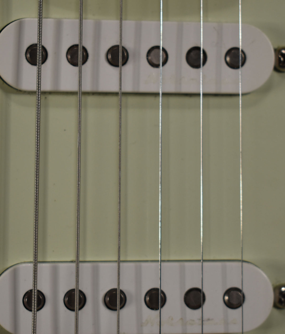 Close-up of a guitar's body, showing two white single-coil pickups with dark pole pieces and six strings running over them.