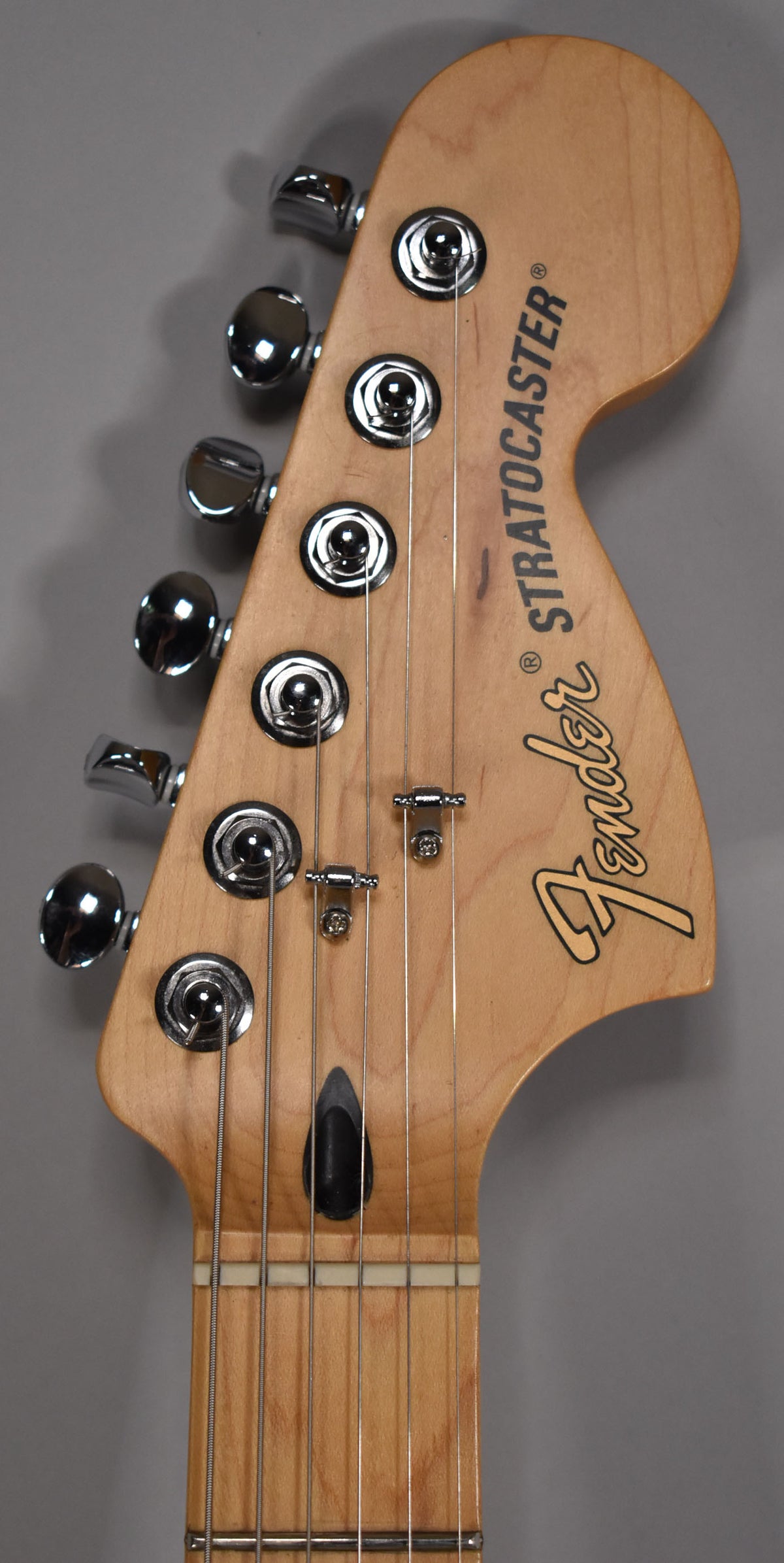 Close-up of the maple headstock and fretboard, showing six chrome tuners, two string trees, and a black truss rod cover.