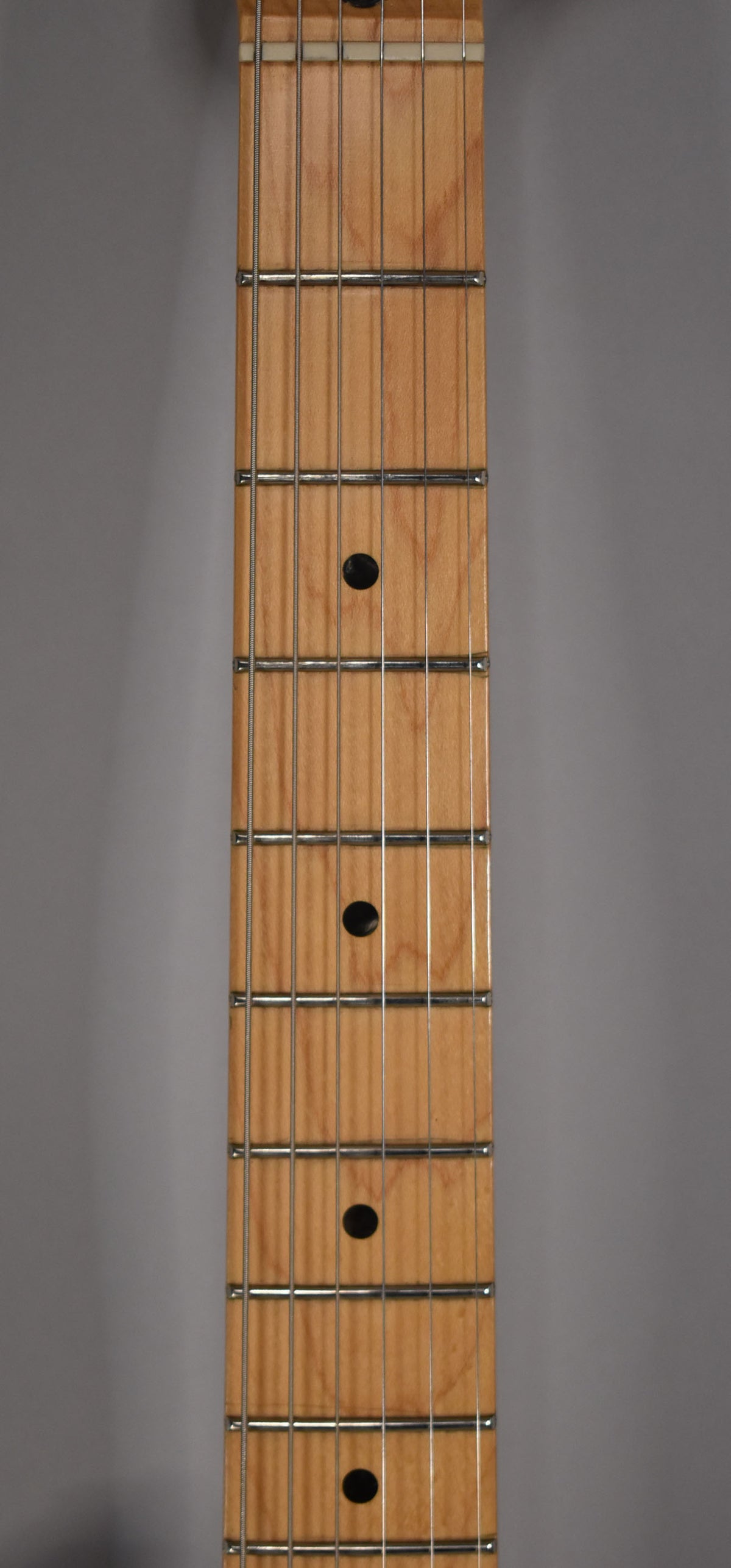 Close-up of the maple fretboard, showing the nut, frets, strings, and four black dot inlays on a light wood grain.