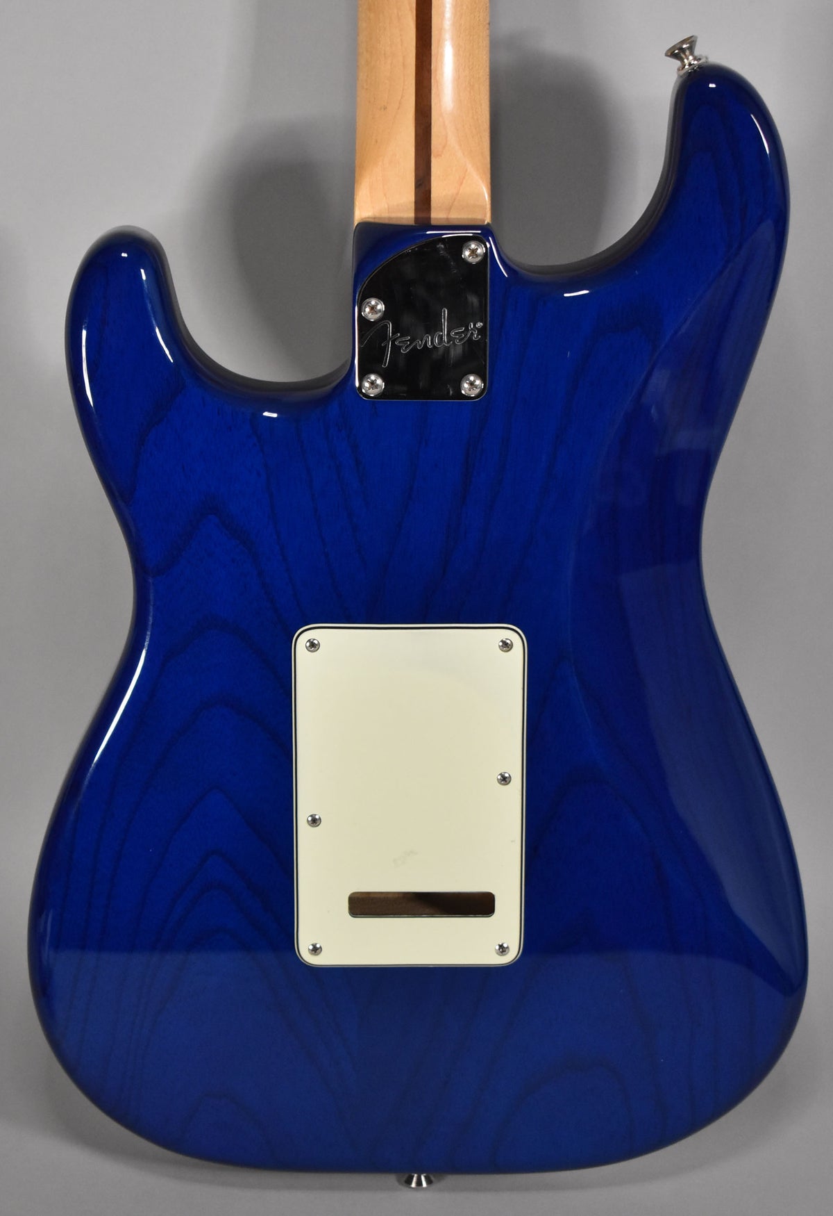 The back of a sapphire blue Stratocaster with a maple neck, showing a cream tremolo cover and chrome neck plate.
