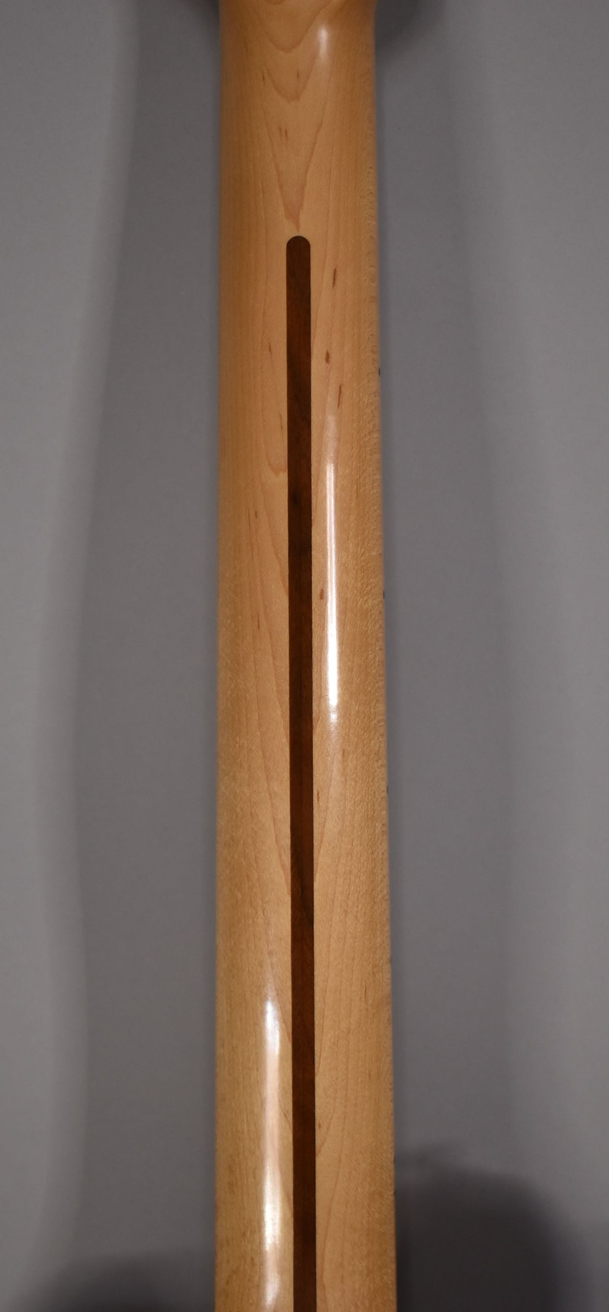 The maple neck's back is shown, with a dark wood skunk stripe and a glossy finish, revealing light wood grain.