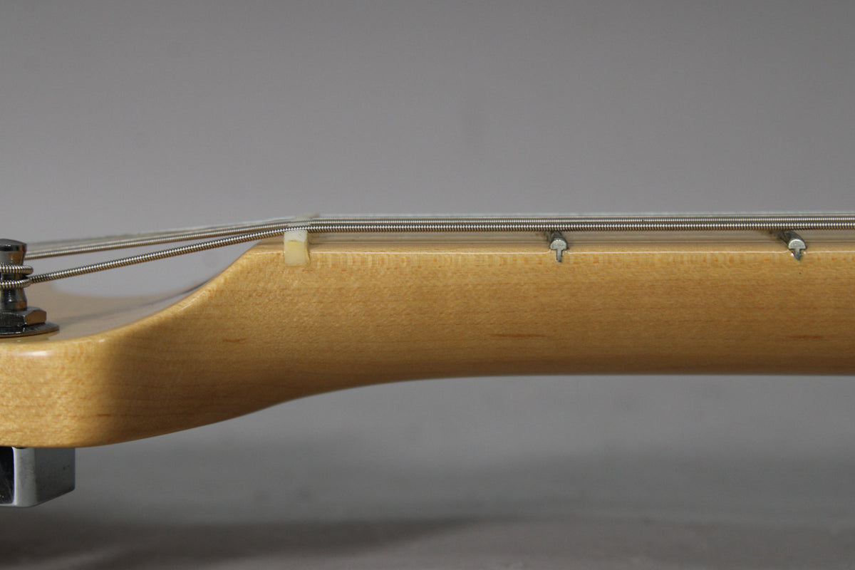Close-up of the light-colored maple neck and headstock transition, showing the nut, string tree, and strings.