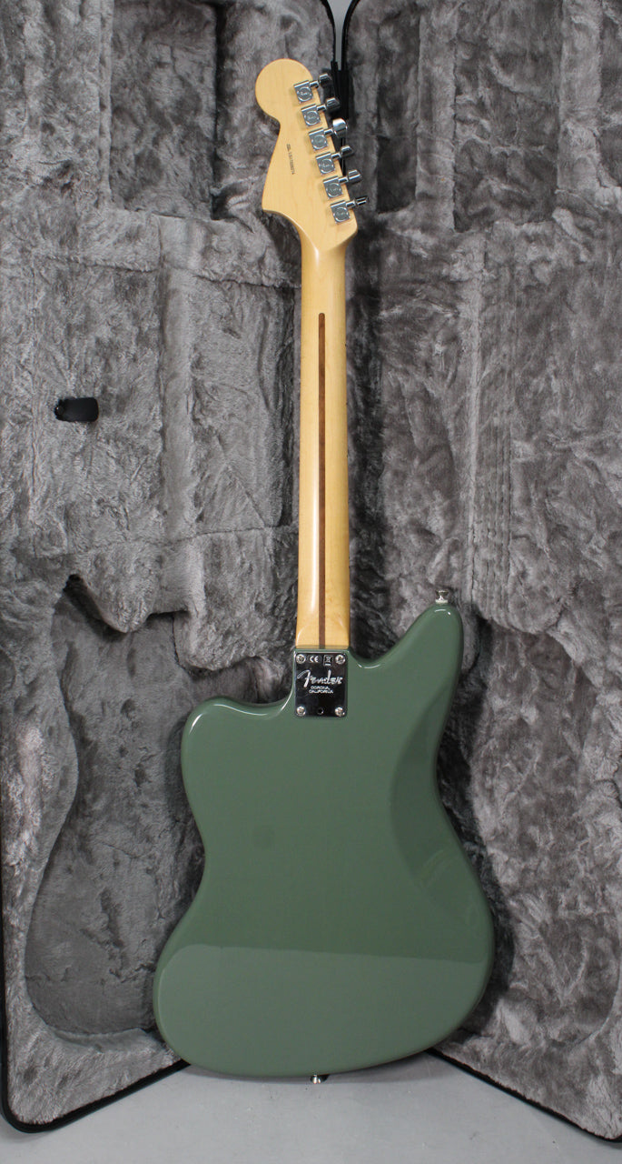 The back of an olive green Jaguar guitar with a maple neck and chrome tuners, resting in a grey plush hard case.