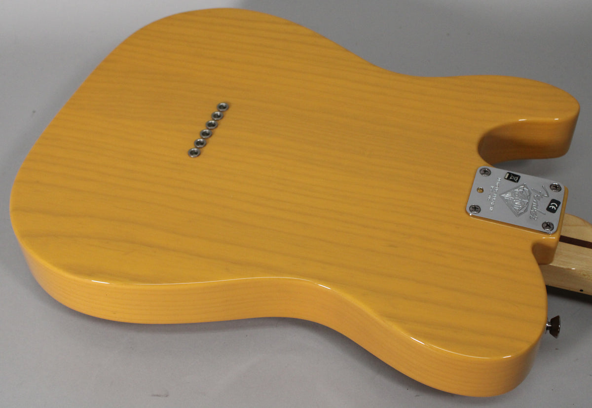 The back of a butterscotch blonde Telecaster body, showing wood grain, string-through ferrules, and a chrome neck plate.