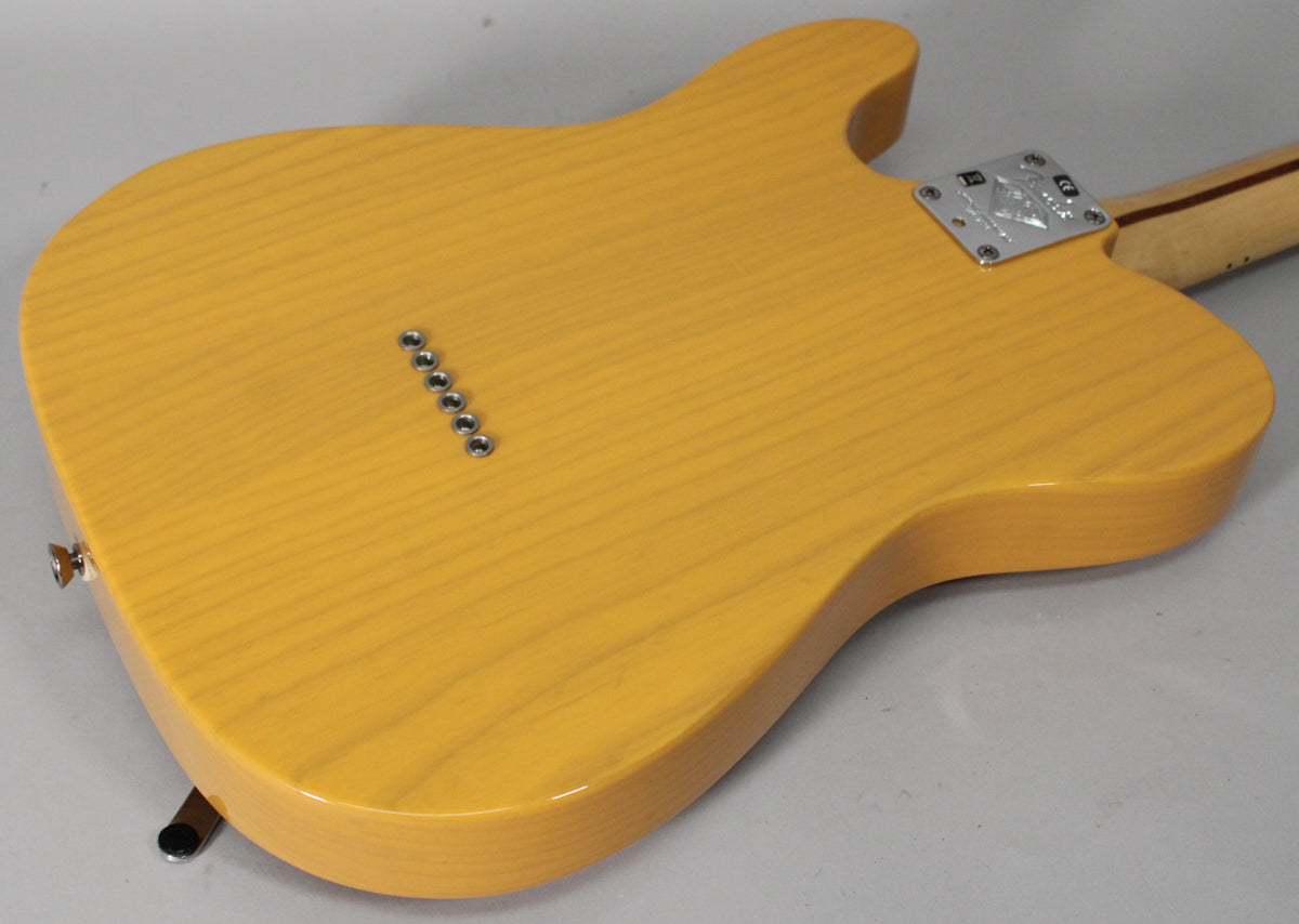 The guitar's butterscotch blonde ash body, with visible wood grain, is seen from the back, showing string-through-body ferrules and neck plate.